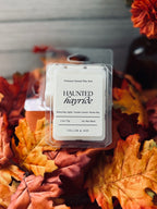 A wax melt package labeled 'Haunted Hayride' by Cellar & Ash, placed on top of autumn leaves. The clear plastic clamshell contains a white wax melt with a white label featuring black text.